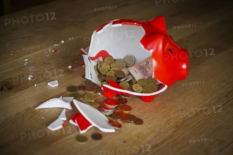 Symbolic photo on the subject of saving. An open, broken piggy bank with coins and banknotes stands on a table. Berlin, 10.02.2024