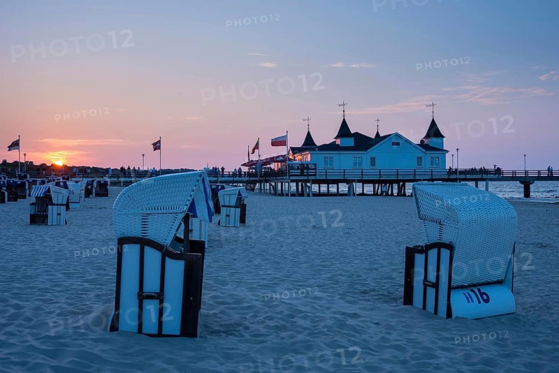 Beach chairs on the sandy beach, people strolling on a pier with buildings in the sunset, clear, blue, cloudless sky, pier Ahlbeck in the last sunlight, view from the eastern beach to the west, seaside resort Ahlbeck, Usedom Island, Mecklenburg-Western Pomerania, Germany, Europe
