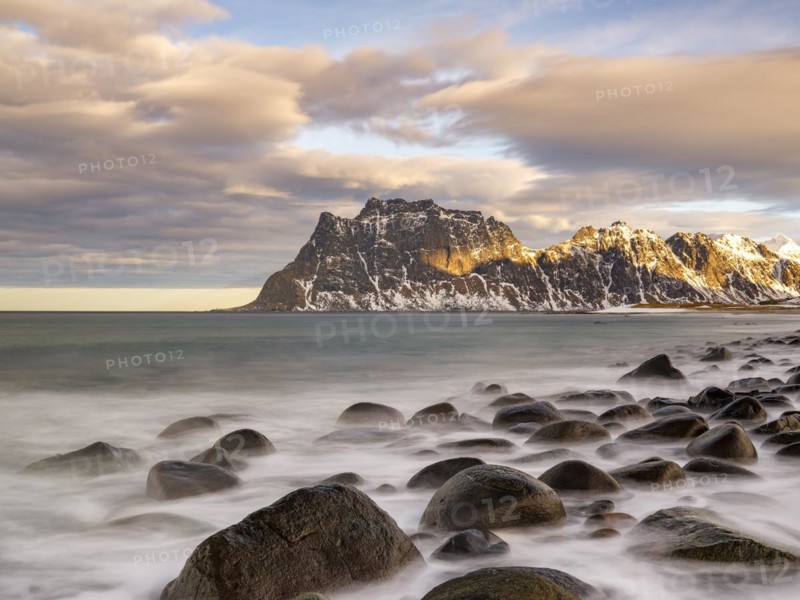 Rounded rocks on Utakleiv beach in a dramatic cloudy atmosphere, snow-capped mountains in the background, Vestvagoya, Lofoten, Norway, Europe