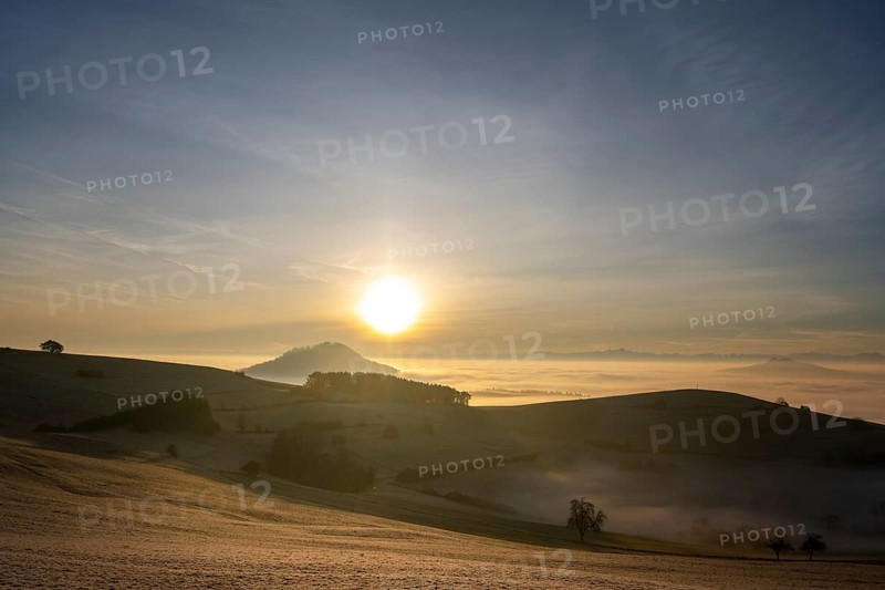View from the old post road near Leipferdingen into the wintry and misty Hegaulandschaft at sunrise, on the horizon the Hohenhewen, on the right the Hohenstoffeln, behind it the Alpine chain, District of Constance, Baden-Württemberg, Germany, Europe