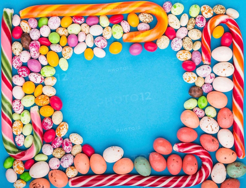 Colorful frame of multicolored candies on a blue background. Christmas cane, chocolate eggs, caramel dragees. Circle copy space, top view, flat lay