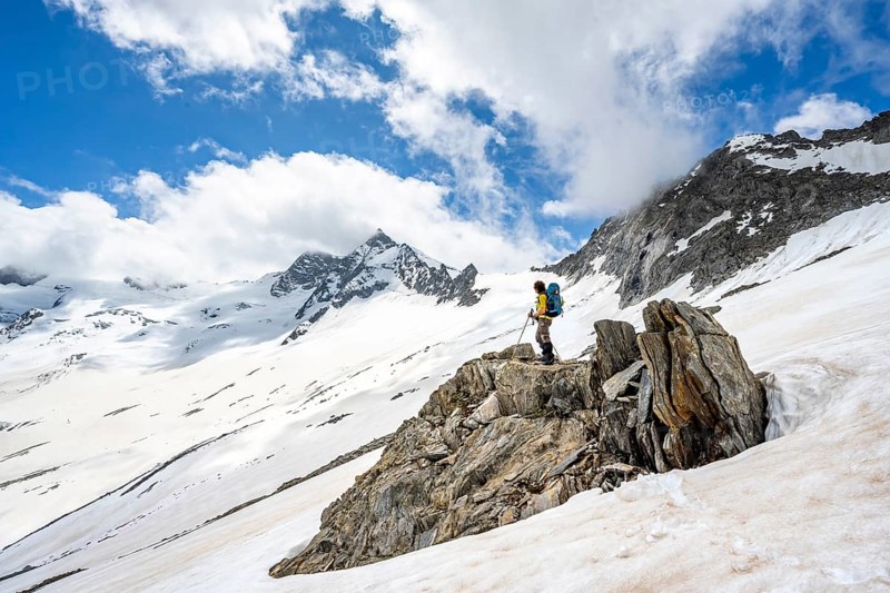 Mountaineer on a rock between snow, descent from the summit of Schönbichler Horn, view of snow-covered and glaciated mountain landscape with summit GroÃŸer Möseler, Berliner Höhenweg, Zillertal Alps, Tyrol, Austria, Europe