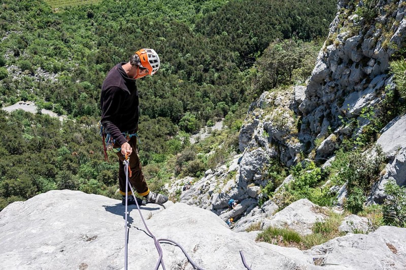 A climber in safety equipment descends a rocky mountain face, alpine climbing with rope, Arco, Italy, AI generated, Europe