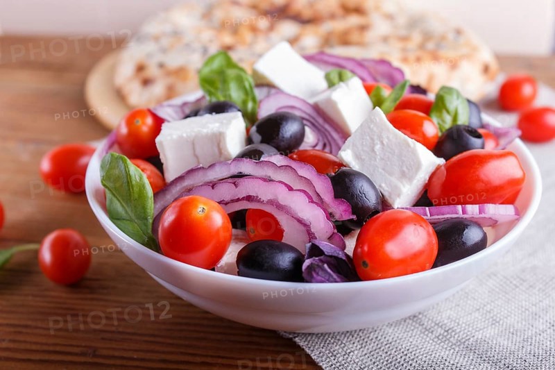 Greek salad with fresh cherry tomatoes, feta cheese, black olives, basil and onion on wooden background, pancake, close up