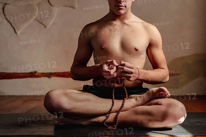 Young unrecognizable man meditating with a rudraksha mala in his hands. Contemplative lifestyle