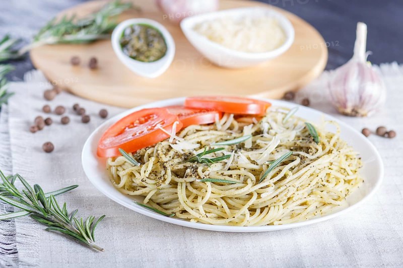 Spaghetti pasta with pesto sauce, tomatoes and cheese on a linen tablecloth. close up, selective focus