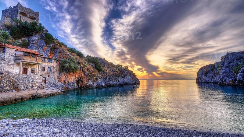 Colourful sunrise on a pebble beach with cliffs and historic building, Mani Peninsula, Peloponnese, Greece, Europe