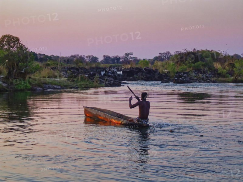 A Kavango fisherman pulls a net through a side arm of the Okavango River in the evening with his mokoro, a dugout canoe. Okavango, Divundu, Kavango West, Namibia, Africa