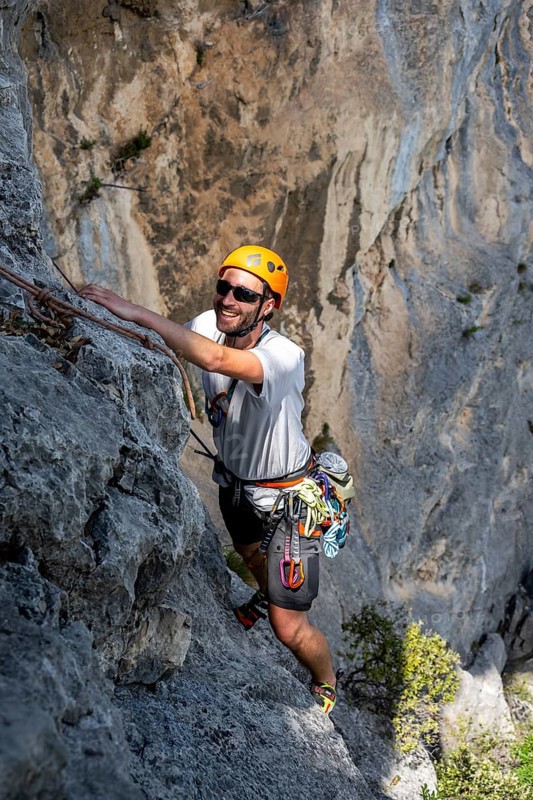 A climber with helmet and safety equipment scales a steep rock face, alpine climbing with rope, Arco, Italy, Europe