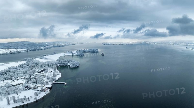Aerial panorama of the snow-covered Mettnau peninsula with the Mettnau park, spa centre and beach café, Reichenau island on the horizon, Radolfzell on Lake Constance, Constance district, Baden-Württemberg, Germany, Europe