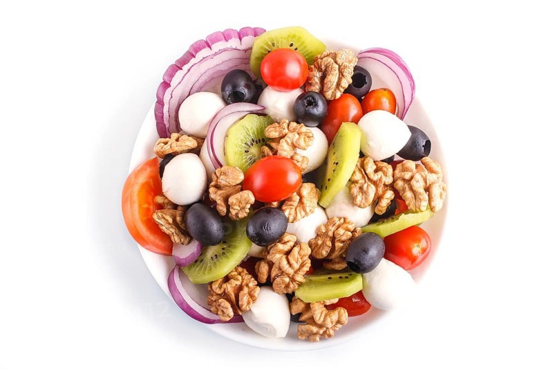 Salad with cherry tomatoes, mozzarella cheese, black olives, kiwi, and walnuts isolated on white background. top view