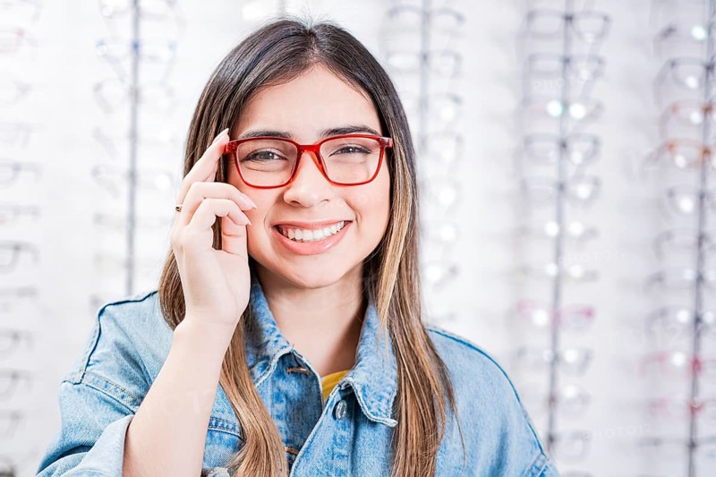 Happy teen girl in eyeglasses on a background of optical store. Happy female customer modeling glasses in an optical store
