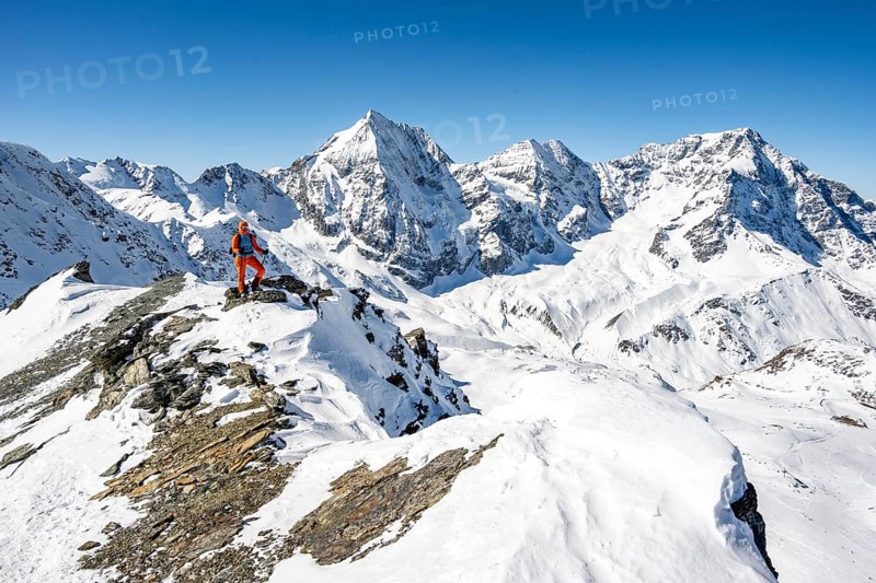 Mountaineer standing on a ledge in front of snow-covered mountains, summit of Madritschspitze, behind Königsspitze, ZebrÃ¹ and Ortler, Ortler Alps, Italy, Europe