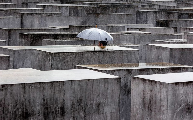 A visitor to the Memorial to the Murdered Jews of Europe protects himself from heavy rain with an umbrella. Berlin, 23.06.2023