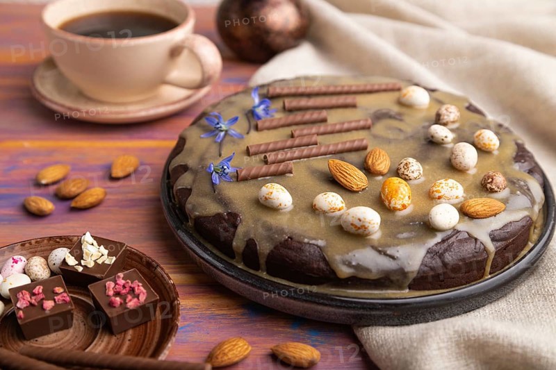 Homemade chocolate brownie cake with caramel cream and almonds with cup of coffee on a colored wooden background and linen textile. Side view, close up, selective focus