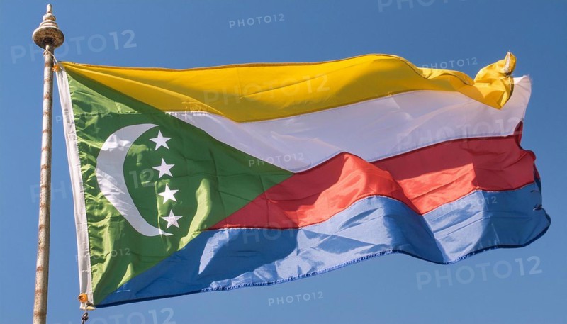 The flag of the Comoros flutters in the wind, isolated against a blue sky