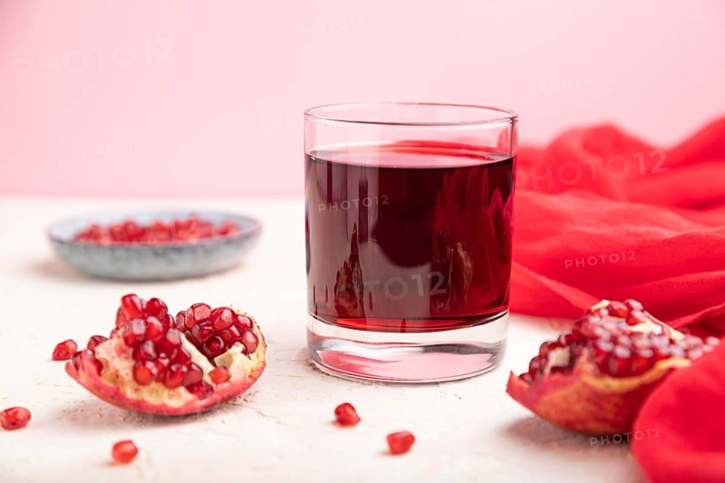 Glass of pomegranate juice on a white and pink background with red textile. Side view, close up, selective focus