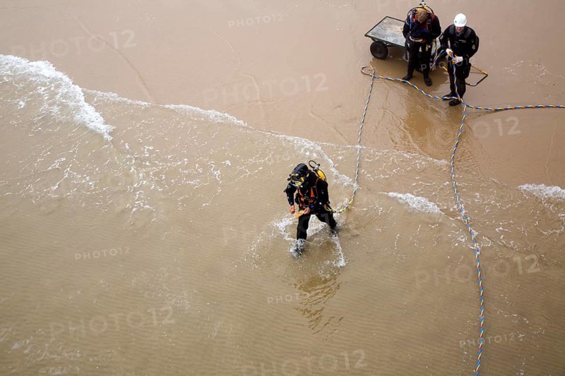 Looking down from above at professional divers on a beach about to enter the sea to work on the pier at Cromer, north Norfolk coast, England, United Kingdom, Europe
