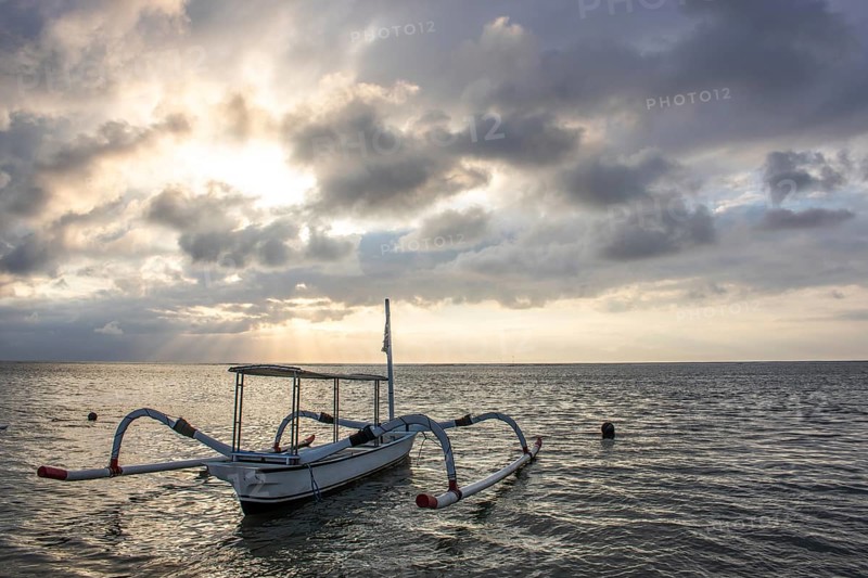 Jukung in the sea, typical landscape shot with a view of the horizon over the water, taken from a sandy beach. Traditional fishing boat at sunrise. Landscape shot of Sanur, Bali, Indonesia, Asia