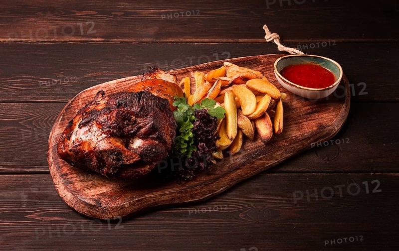 Pork knuckle, in soy-honey sauce, with fried potatoes, on a wooden chopping board, homemade, no people