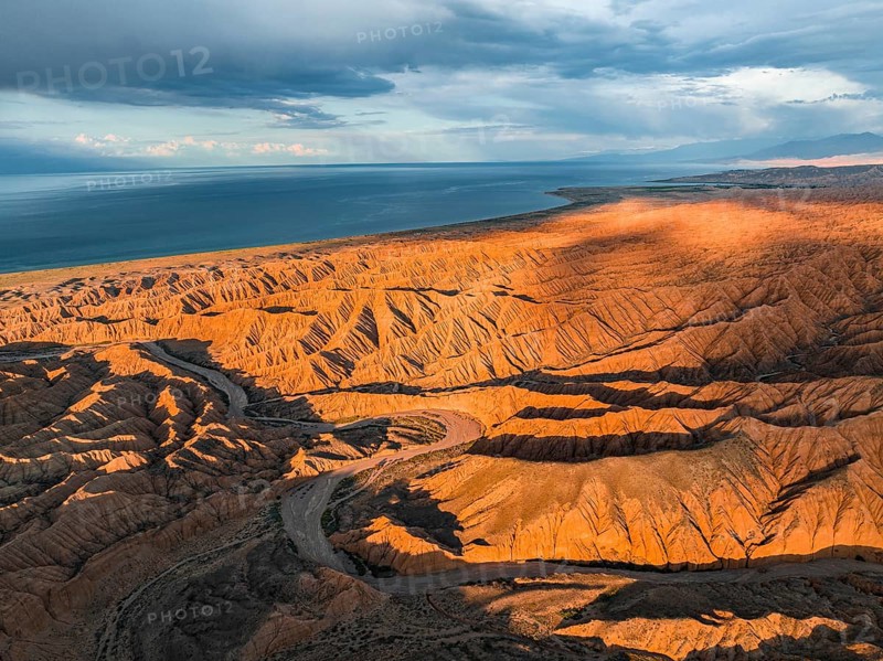 Riverbed runs through a landscape of eroded hills, badlands at sunset, Issyk Kul Lake in the background, aerial view, Canyon of the Forgotten Rivers, Issyk Kul, Kyrgyzstan, Asia