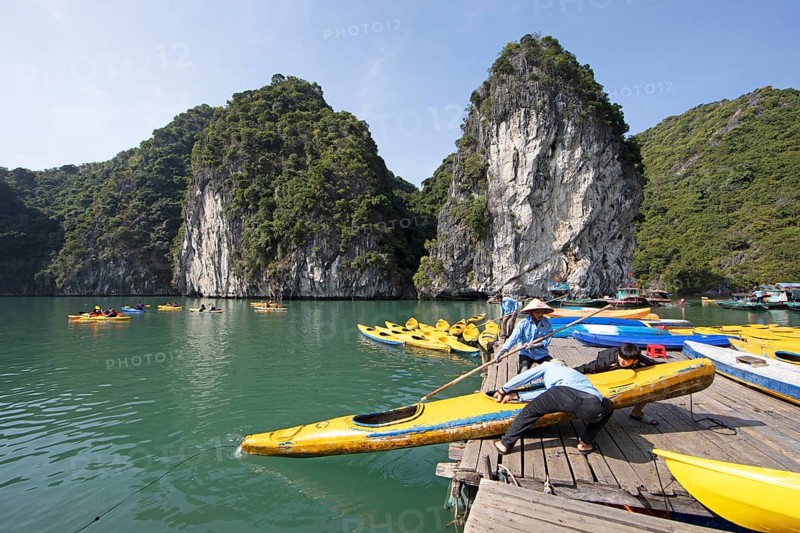 Vietnamese men pull a kayak onto a jetty, behind them the karst rocks of Lan Ha Bay, Halong Bay, Vietnam, Asia