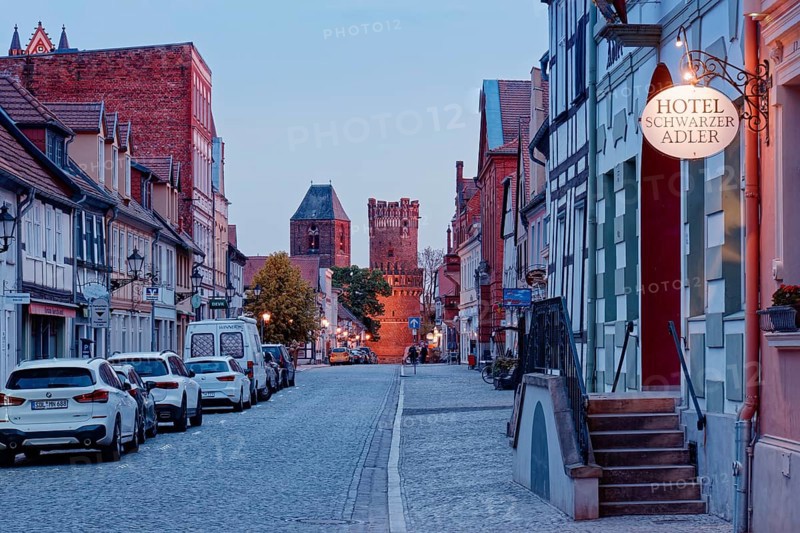 The Lange StraÃŸe with half-timbered houses and other old buildings, covered with cobblestones, illuminated in the evening. The NeustÃ¤dter Tor in the background. Old town centre of Tangermünde, Hanseatic town in the Altmark. Saxony-Anhalt, Germany, Europe
