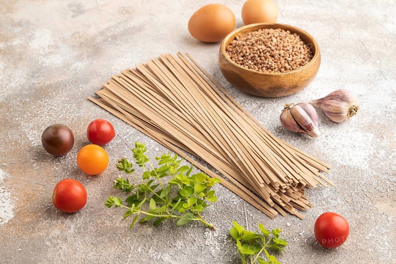Japanese buckwheat soba noodles with tomato, eggs, spices, herbs on brown concrete background. Side view, close up