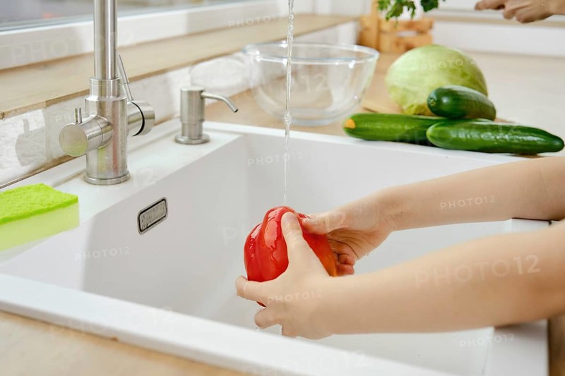 Closeup view of hands of kid washing bell pepper in the sink