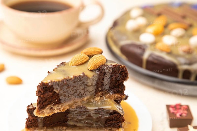 Pieces of chocolate brownie cake with caramel cream and almonds on a white concrete background. Side view, close up, selective focus