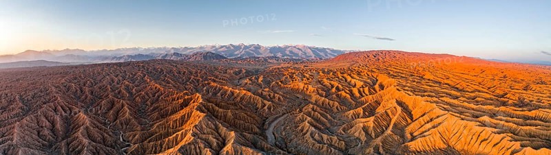 Panorama, riverbed runs through a landscape of eroded hills, badlands at sunrise, mountain peaks of the Tien Shan Mountains in the background, aerial view, Canyon of the Forgotten Rivers, Issyk Kul, Kyrgyzstan, Asia
