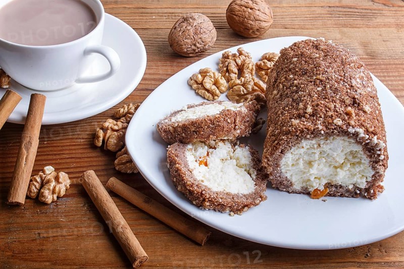 Roll cake with curd and walnuts isolated on brown wooden background, close up