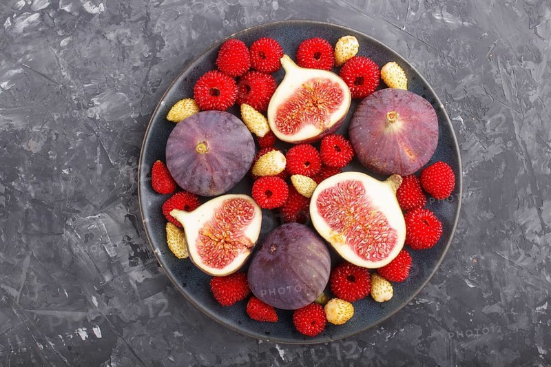 Fresh figs, strawberries and raspberries on blue ceramic plate on black concrete background. top view, flat lay, close up