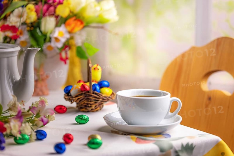 A coffee cup on a table with Easter decorations and a colourful bouquet of spring flowers in the background