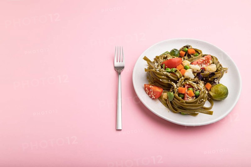 Tagliatelle green spinach pasta with tomato, pea and microgreen sprouts on a pastel pink background. Side view, close up, copy space