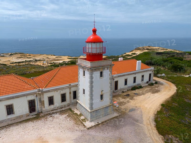 Close-up of a lighthouse and a neighbouring building overlooking the sea under a cloudy sky Aerial view, Farol do Cabo Sardao, Sardao, Ponta do Cavaleiro, Odemira, Alentejo, Portugal, Europe
