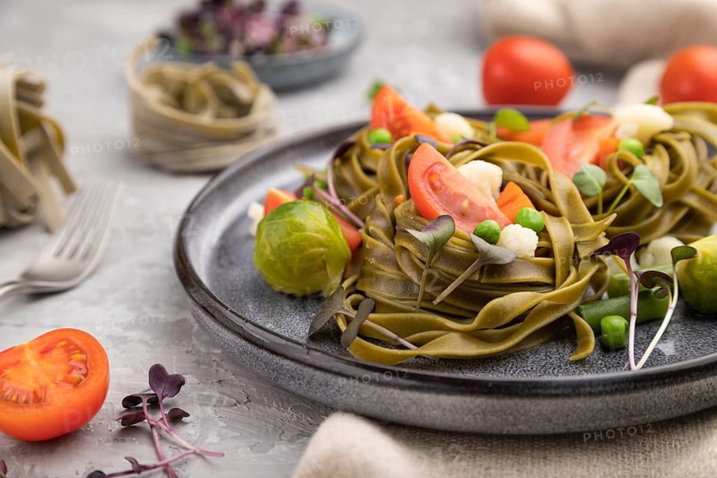 Tagliatelle green spinach pasta with tomato, pea and microgreen sprouts on a gray concrete background and linen textile. Side view, close up, selective focus