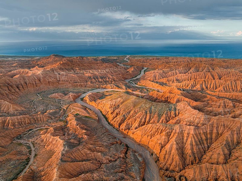 Riverbed runs through a landscape of eroded hills, badlands at sunset, Issyk Kul Lake in the background, aerial view, Canyon of the Forgotten Rivers, Issyk Kul, Kyrgyzstan, Asia
