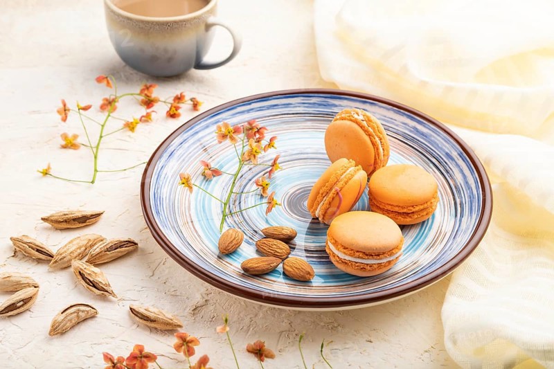 Orange macarons or macaroons cakes with cup of coffee on a white concrete background and linen textile. Side view, close up