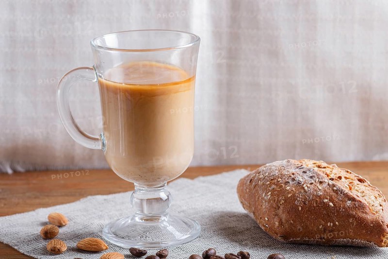 Glass cup of coffee with cream and bun on a wooden background and linen textile. close up, copy space