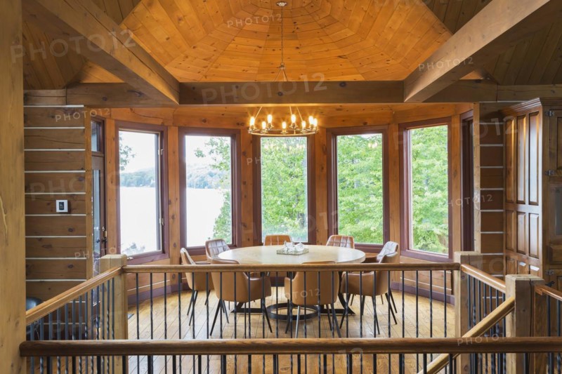 Staircase and round wooden dining table with tan leather armchairs in dining room inside a milled Eastern white pine timber and flat log profile home, Quebec, Canada. This image is property released. CUPR0362