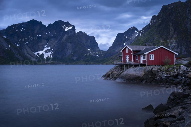 A typical red wooden house on wooden stilts (rorbuer) in the small village of Toppoya (Toppoy) . View of the sea and the mountains. At night during the midnight sun. Long exposure.Toppoya, Moskenesoya, Lofoten, Norway, Europe