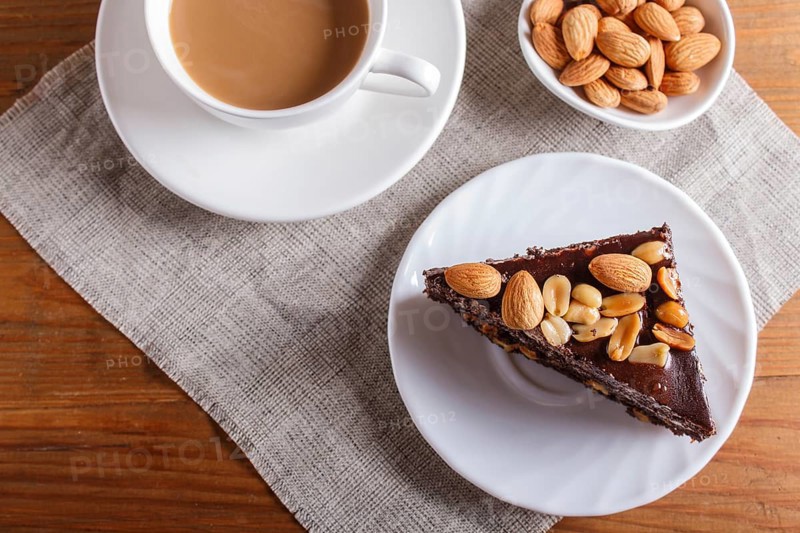 Chocolate cake with caramel, peanuts and almonds on a brown wooden background. cup of coffee, top view, close up