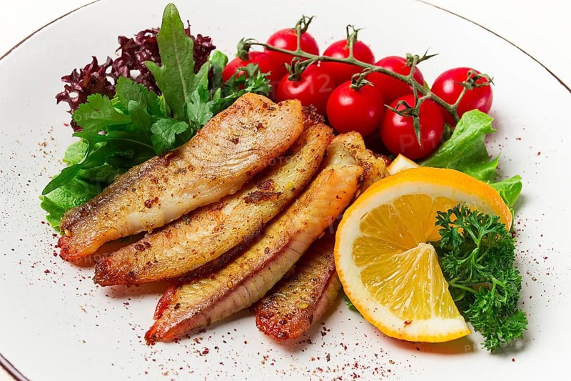 Fried Tilapia fish fillet, in spices, with cherry and salad, on a white plate, homemade, no people