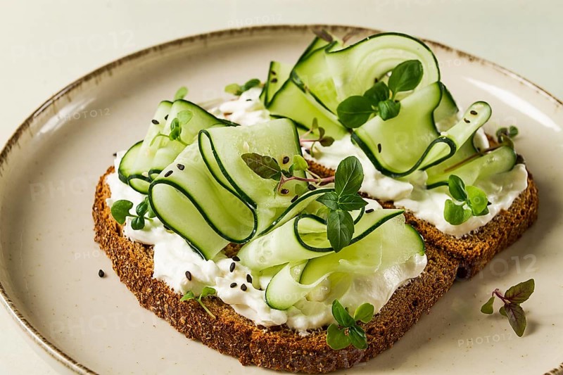Breakfast, cereal bread sandwiches, cream cheese, sliced cucumber, with micro greenery on a light table, close-up, top view, selective focus, no people