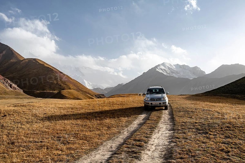 Off-road vehicle on a track between yellow meadows, glaciated high mountain peaks in the background, Lenin Peak, Trans Alay Mountains, Pamir Mountains, Osh Province, Kyrgyzstan, Asia