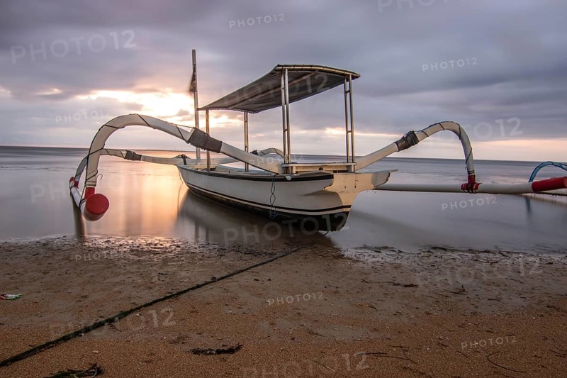 Jukung in the sea, typical landscape shot with a view of the horizon over the water, taken from a sandy beach. Traditional fishing boat at sunrise. Landscape shot of Sanur, Bali, Indonesia, Asia