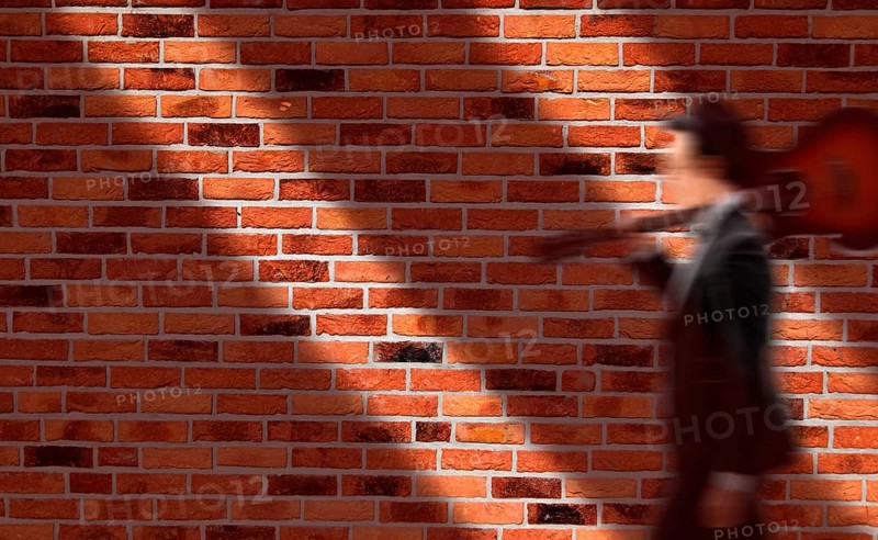 House wall with red bricks, musician carries his guitar on his shoulder, motion blur