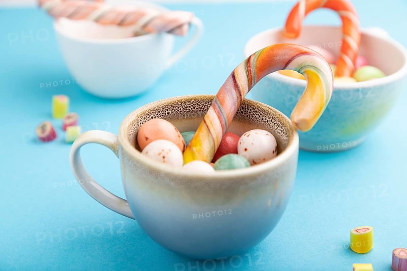 Heap of multicolored caramel candies in cups on blue pastel background. close up, side view, selective focus