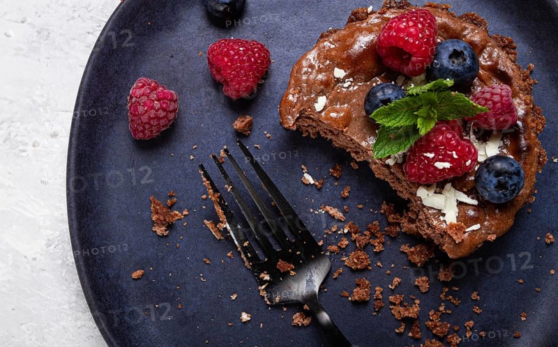 Half-eaten chocolate tartlet, on a plate, stuffed with cottage cheese and berries, breakfast, homemade, no people